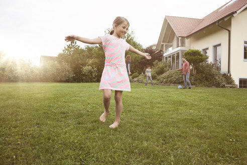 Mädchen tanzt im Garten mit Familie im Hintergrund - RBF005108