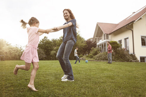 Mutter und Tochter tanzen im Garten mit der Familie im Hintergrund - RBF005109