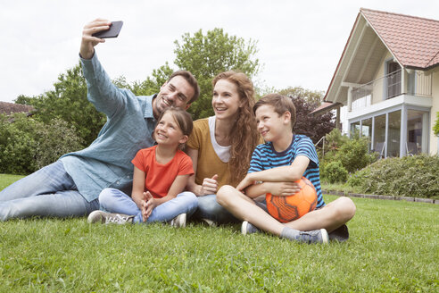 Lächelnde Familie sitzt im Garten und macht ein Selfie - RBF005128