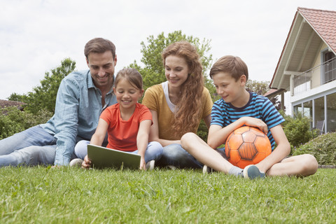 Smiling family sitting in garden with football using tablet stock photo