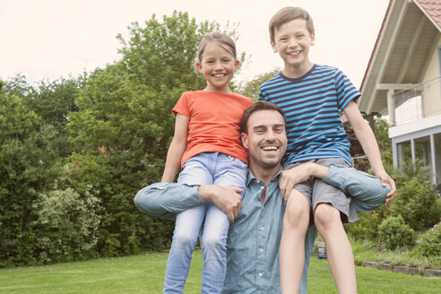 Porträt eines glücklichen Vaters, der seine beiden Kinder im Garten trägt - RBF005136