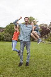 Portrait of happy father carrying his two children in garden - RBF005137