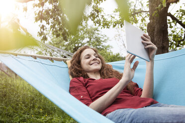Smiling woman in hammock using tablet - RBF005147