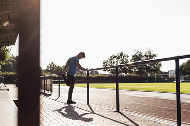 Sportler beim Dehnen in einem Leichtathletikstadion - UUF008287