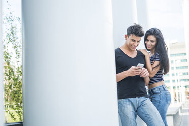 Smiling young couple outdoors looking at cell phone - SIPF000799