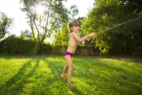 Kleines Mädchen spritzt Wasser mit Wasserpistole, lizenzfreies Stockfoto