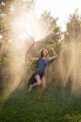 Girl dancing while splashing water with garden hose - LVF005238