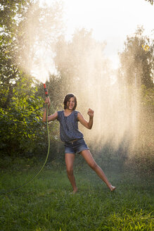 Mädchen singt und tanzt, während sie mit einem Gartenschlauch Wasser verspritzt - LVF005239