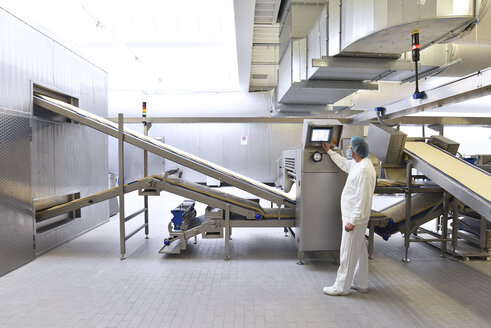 Arbeiter bei der Bedienung einer Maschine in einer industriellen Bäckerei - LYF000552