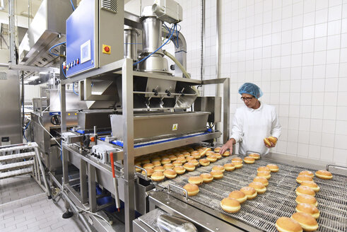 Worker at production line in a baking factory with Berliners - LYF000553