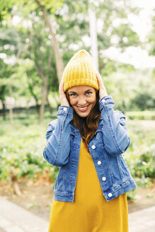 Porträt einer lächelnden jungen Frau, die eine gelbe Mütze aufsetzt - EBSF001676