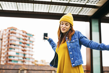 Young woman with yellow cap dancing while listening music with earphones - EBSF001678