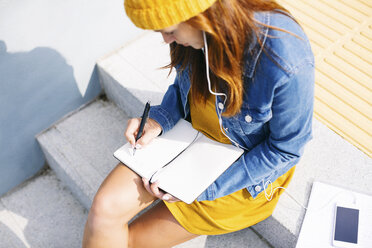 Young woman sitting on steps writing down something - EBSF001687