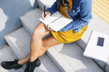 Young woman sitting on steps writing down something, partial view - EBSF001688