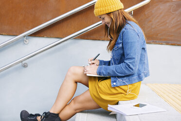 Junge Frau sitzt auf einer Treppe und schreibt etwas auf - EBSF001690