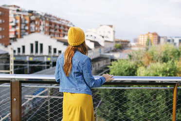 Rückenansicht einer jungen Frau mit gelber Mütze und Blick auf die Umgebung - EBSF001693