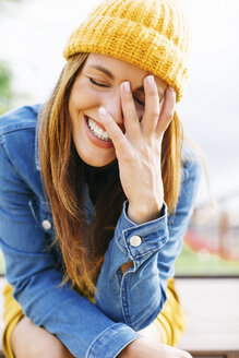 Porträt einer lachenden jungen Frau mit Hand im Gesicht - EBSF001697
