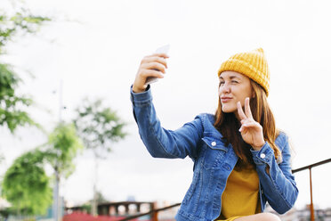 Smiling young woman showing victory sign while taking selfie - EBSF001700