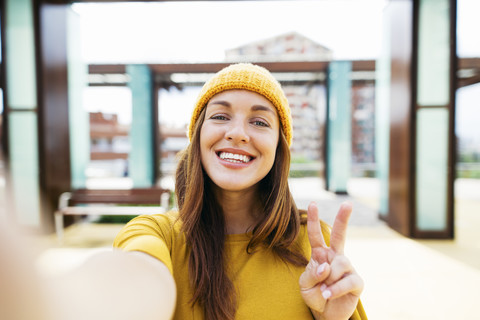 Porträt einer lächelnden jungen Frau in gelber Kleidung, die ein Selfie macht, lizenzfreies Stockfoto