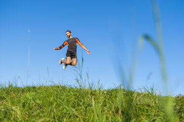 Athlete jumping on meadow under blue sky - DIGF001075