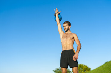 Mann trainiert mit Kettlebell unter blauem Himmel - DIGF001088