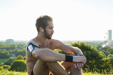 Athlete sitting on a meadow listening to music after workout - DIGF001094