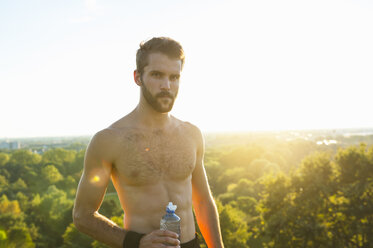 Athlet mit nacktem Oberkörper hält Wasserflasche bei Sonnenuntergang - DIGF001100