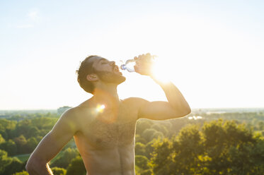 Athlet mit nacktem Oberkörper trinkt bei Sonnenuntergang aus einer Flasche - DIGF001101