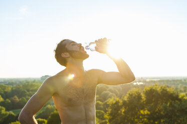 Barechested athlete drinking from bottle at sunset - DIGF001101