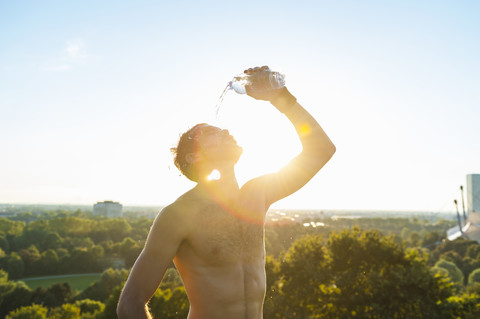 Athlet mit nacktem Oberkörper, der sich bei Sonnenuntergang Wasser über das Gesicht gießt, lizenzfreies Stockfoto