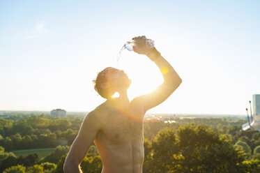 Athlet mit nacktem Oberkörper, der sich bei Sonnenuntergang Wasser über das Gesicht gießt - DIGF001102