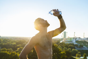 Barechested athlete pouring water over his face at sunset - DIGF001103