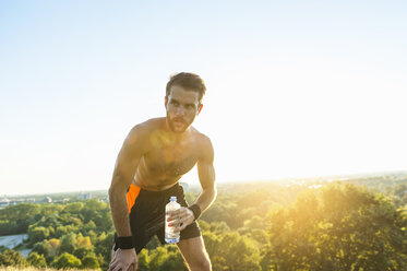 Athlet mit nacktem Oberkörper hält Wasserflasche bei Sonnenuntergang - DIGF001105