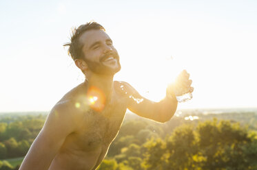 Glücklicher Athlet mit nacktem Oberkörper, der sich bei Sonnenuntergang Wasser über den Körper gießt - DIGF001107