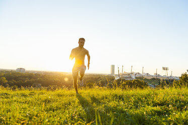 Barechested man running on meadow in park at sunset - DIGF001109