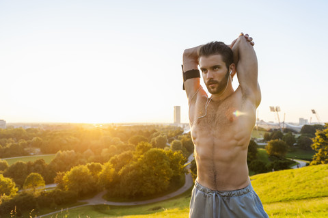 Athlet mit nacktem Oberkörper dehnt sich bei Sonnenuntergang, lizenzfreies Stockfoto