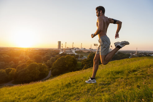 Mann mit nacktem Oberkörper läuft auf einer Wiese im Park bei Sonnenuntergang - DIGF001124