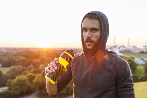 Sportler hält Flasche bei Sonnenuntergang, lizenzfreies Stockfoto