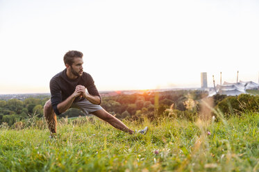 Athlete stretching on meadow at sunset - DIGF001133