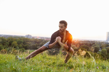 Sportler beim Dehnen auf einer Wiese bei Sonnenuntergang - DIGF001134