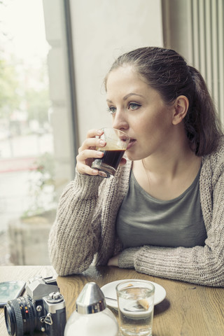 Junge Frau mit Kamera beim Kaffeetrinken in einem Cafe, lizenzfreies Stockfoto