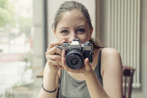 Porträt einer lächelnden jungen Frau, die eine Kamera hält, lizenzfreies Stockfoto