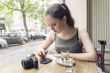 Junge Frau in einem Café mit Kamera, die ihr Mobiltelefon überprüft - TAMF000601