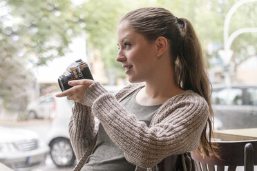Junge Frau hält eine Kamera hinter einer Fensterscheibe - TAMF000604