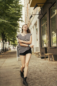 Germany, Berlin, laughing young woman walking on pavement - TAMF000611