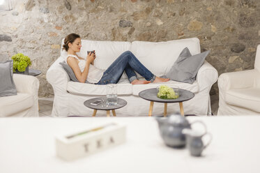 Woman sitting on couch, drinking tea - DIGF001171