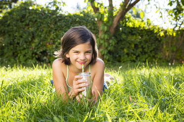 Porträt eines kleinen Mädchens, das auf einer Wiese liegt und einen Smoothie trinkt - LVF005257