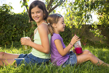 Two little sisters sitting back to back on a meadow drinking smoothies - LVF005258
