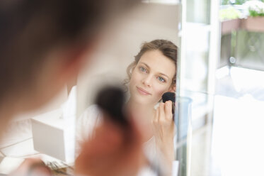 Woman looking in mirror applying eye makeup - DIGF001179