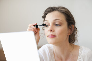 Woman looking in mirror applying mascara - DIGF001180